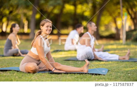 Yoga lesson visitors with coach perform Parivritta Janu Shirshasana in park Yoga lesson visitors with coach perform Parivritta Janu Shirshasana in park 117587837