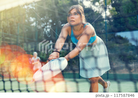 Athletic woman plays padel outdoor. View through tennis net Athletic woman plays padel outdoor. View through tennis net 117587846