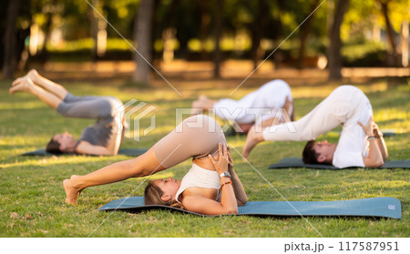 Yoga lesson visitors with coach perform plow pose in park Yoga lesson visitors with coach perform plow pose in park 117587951