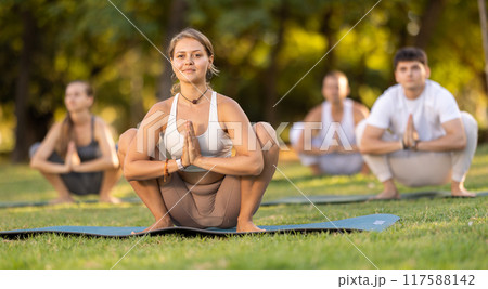 Girl performing Garland Pose during group yoga in summer park Girl performing Garland Pose during group yoga in summer park 117588142