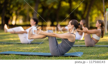 Woman participating in outdoor group yoga session in city park 117588143