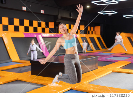 Portrait of joyful young woman in sport clothes enjoying weekend time on trampolines in entertainment center 117588230