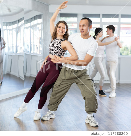 Positive girl dancing playful bachata with partner in studio 117588260