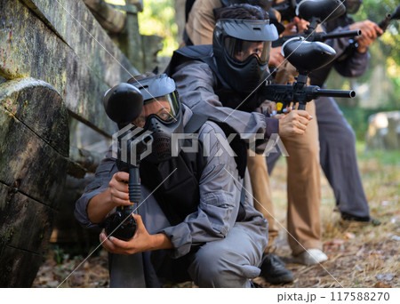 Group of paintball players aiming and shooting with guns outdoors Group of paintball players aiming and shooting with guns outdoors 117588270