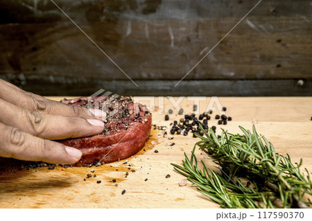 A hand is seasoning a tenderloin meat with pepper and salt 117590370