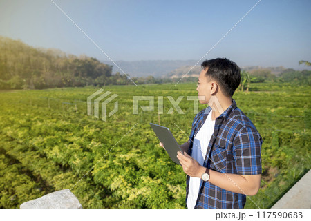 A man wearing a watch is looking at a field of green plants A man wearing a watch is looking at a field of green plants 117590683