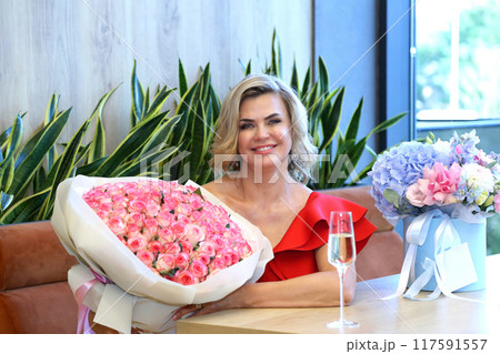 Beautiful woman in a red dress. Beautiful mature woman with champagne. A gorgeous adult beauty in a red dress with flowers and champagne. Gorgeous adult beauty. Beautiful woman in a red dress. Beautiful mature woman with champagne. A gorgeous adult beauty in a red dress with flowers and champagne. Gorgeous adult beauty. 117591557