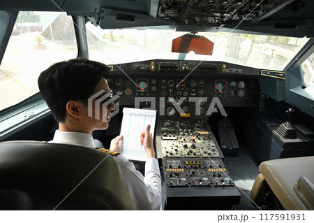Back view of asian pilot dressed in a uniform preparing for flight in the cockpit of an aircraft Back view of asian pilot dressed in a uniform preparing for flight in the cockpit of an aircraft 117591931