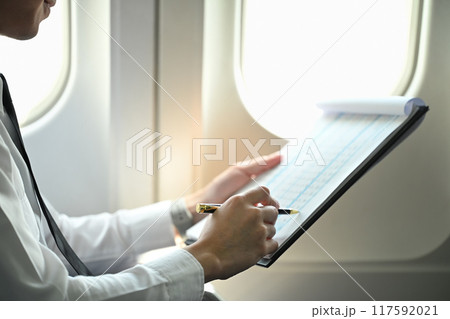 Close up image of pilot reviewing flight plans or other important information while sitting in an airplane cabin 117592021