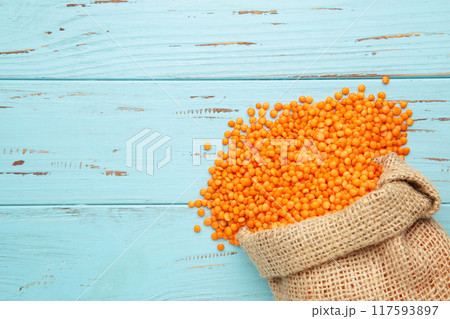 Red lentils in bag on blue wooden background. Red lentils in bag on blue wooden background. 117593897