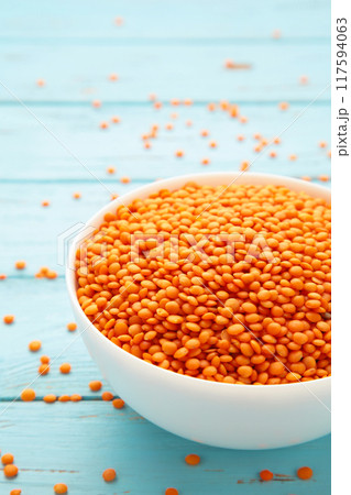 Red lentils in white bowl on a blue wooden table. Red lentils in white bowl on a blue wooden table. 117594063