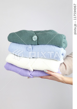 Stack of cozy knitted sweaters in hand on light background. Stack of cozy knitted sweaters in hand on light background. 117594067