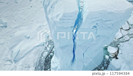 Blue high cracked iceberg towering in frozen Antarctica polar ocean. Huge snow covered ice glacier in wild nature environment icy landscape. Discover South Pole beauty. Aerial drone close up view 117594384