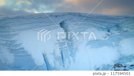 Towering ice cliff in sunset Antarctic landscape, toward colorful sky. Breathtaking scene of an Antarctica iceberg. Arctic environment preserve of ice. Huge high glacier at polar nature. Aerial shot Towering ice cliff in sunset Antarctic landscape, toward colorful sky. Breathtaking scene of an Antarctica iceberg. Arctic environment preserve of ice. Huge high glacier at polar nature. Aerial shot 117594501