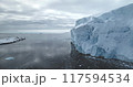 Massive glacier in Antarctica peacefully floats polar ocean. Towering snow covered iceberg rises above cold, dark water. Ice wall formation under moody sky. Antarctica winter landscape panorama 117594534