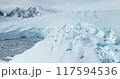 Giant calving glacier towering polar ocean in Antarctica. Snow covered blue iceberg ice wall rises above cold dark water. Antarctic winter landscape panorama. Aerial drone shot cinematic ecology scene 117594536
