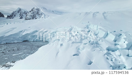 Giant calving glacier towering polar ocean in Antarctica. Snow covered blue iceberg ice wall rises above cold dark water. Antarctic winter landscape panorama. Aerial drone shot cinematic ecology scene 117594536