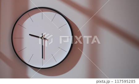 Elegant Black Clock Showing 21.30/09.30 with Shadows on Minimalist Wall - Ideal for Time Management and Interior Design Promotions Elegant Black Clock Showing 21.30/09.30 with Shadows on Minimalist Wall - Ideal for Time Management and Interior Design Promotions 117595285