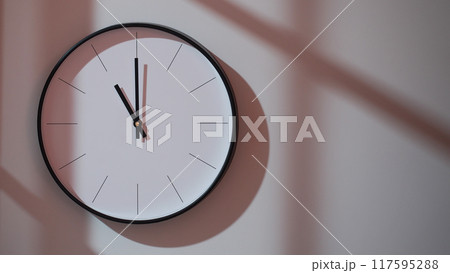 Elegant Black Clock Showing 23.00/11.00 with Shadows on Minimalist Wall - Ideal for Time Management and Interior Design Promotions 117595288