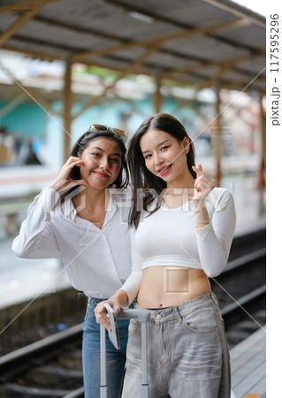 Two women are posing for a picture with their cell phones 117595296