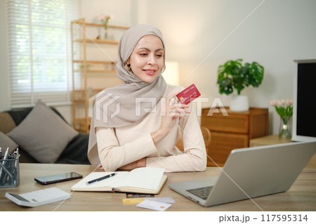 A woman wearing a head scarf is holding a red Visa card 117595314