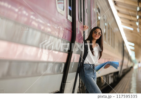A woman is standing in front of a train with a backpack and a blue book A woman is standing in front of a train with a backpack and a blue book 117595335
