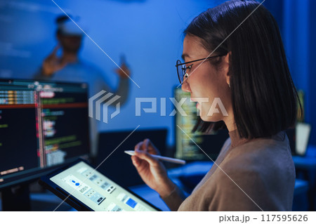 Asian UX designer works on a tablet while a colleague tests a VR application ,integration of user experience design and virtual reality development in a modern tech workspace 117595626