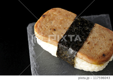 スレートプレートに乗ったスパムむすびを黒背景で撮影 117596043