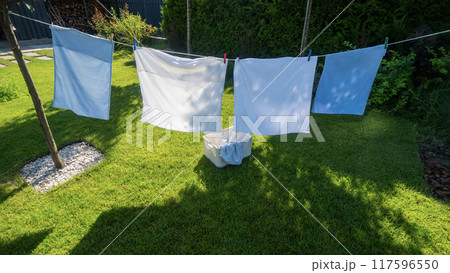 Colorful pillowcases sway on clotheslines in a peaceful backyard, with a well-kept green lawn beneath. 117596550