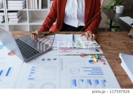 woman meticulously plans a finance audit, using a computer and calculator to review budget documents and ensure accuracy 117597926