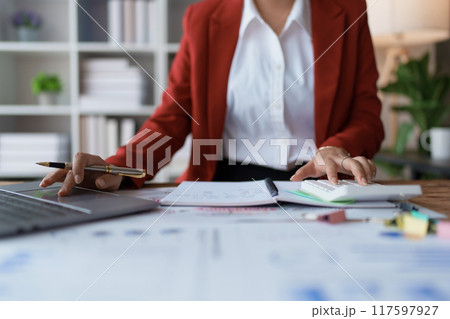 woman meticulously plans a finance audit, using a computer and calculator to review budget documents and ensure accuracy 117597927
