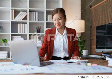 woman meticulously plans a finance audit, using a computer and calculator to review budget documents and ensure accuracy 117597928