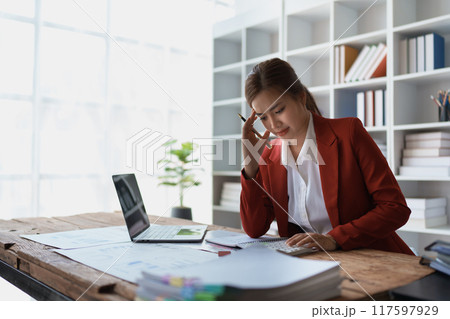 woman meticulously plans a finance audit, using a computer and calculator to review budget documents and ensure accuracy 117597929
