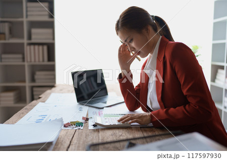 woman meticulously plans a finance audit, using a computer and calculator to review budget documents and ensure accuracy 117597930