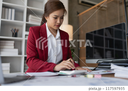 woman meticulously plans a finance audit, using a computer and calculator to review budget documents and ensure accuracy woman meticulously plans a finance audit, using a computer and calculator to review budget documents and ensure accuracy 117597935