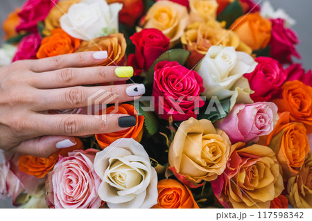Elegant hand with colorful nails resting on a vibrant bouquet of roses Elegant hand with colorful nails resting on a vibrant bouquet of roses 117598342