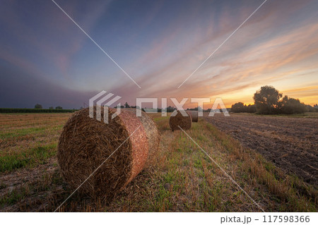 Sunset over a rural field with a bale of hay 117598366