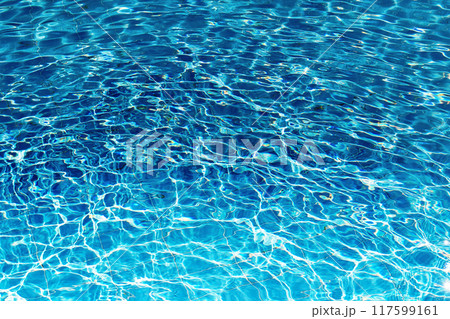 Close-up of a swimming pool filled with clear blue water. Sunlight dances on the surface, creating ripples and sparkling reflections 117599161