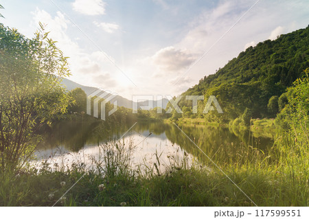 Beautiful summer morning landscape. Clear water mountains lake, blue cloudy sky, sun rays. Beautiful summer morning landscape. Clear water mountains lake, blue cloudy sky, sun rays. 117599551