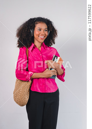 Happy African American woman wearing headphones, holding books, enjoying music and learning. Happy African American woman wearing headphones, holding books, enjoying music and learning. 117599622
