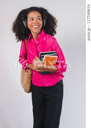 Happy African American woman wearing headphones, holding books, enjoying music and learning. Happy African American woman wearing headphones, holding books, enjoying music and learning. 117599624