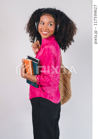 Happy African American woman wearing headphones, holding books, enjoying music and learning. Happy African American woman wearing headphones, holding books, enjoying music and learning. 117599627