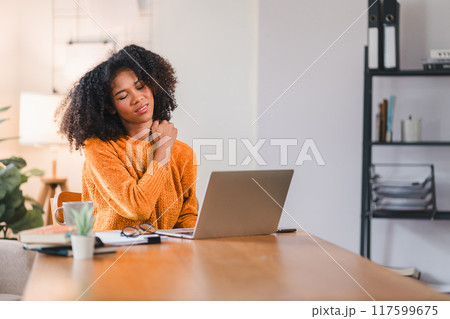 African American woman massaging her neck, indicating discomfort or strain while working on a laptop at home. 117599675