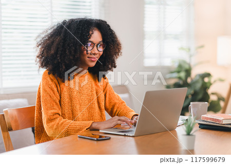 Happy African American woman wearing glasses working on laptop at home. Happy African American woman wearing glasses working on laptop at home. 117599679