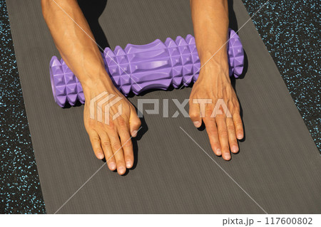 Athlete mans hands exercising and stretching arms on foam roller on sports ground. Outdoor activity. Close up. Athlete mans hands exercising and stretching arms on foam roller on sports ground. Outdoor activity. Close up. 117600802