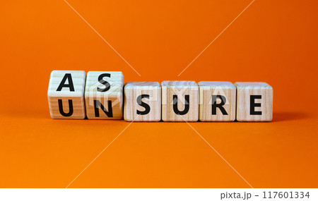 Assure or unsure symbol. Turned wooden cubes and changed the concept word unsure to assure. Beautiful orange table, orange background, copy space. Business and assure or unsure concept. 117601334