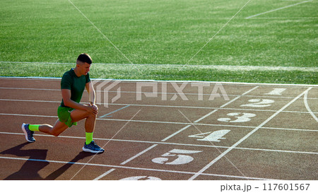 Young fit man in sportswear training on sport arena outdoor, before running, marathon. Athlete stretching legs. 117601567