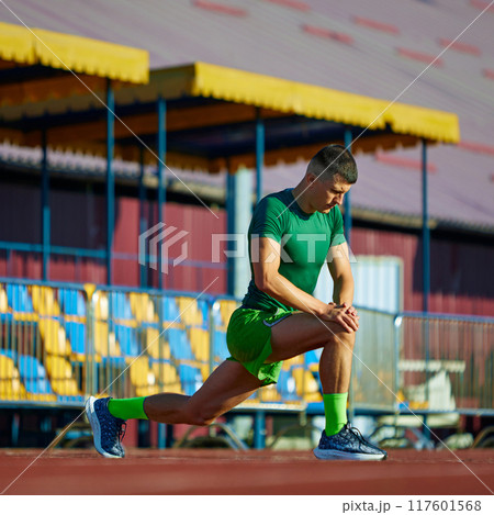 Young athletic man stretching legs before marathon on field outdoor. Training session on start line. 117601568