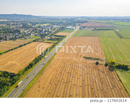 Aerial perspective showing a highway bordered by fields of hay bales, with rural landscape stretching into the distance. 117601614