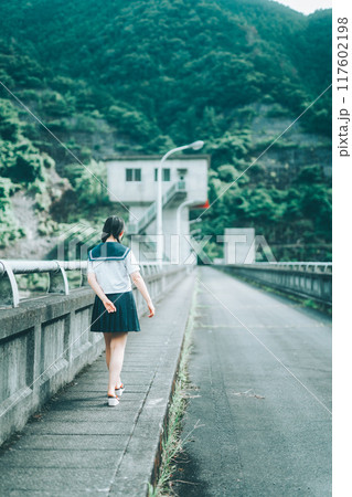 橋の上の道路を歩いてくセーラー服の女の子の後ろ姿 117602198